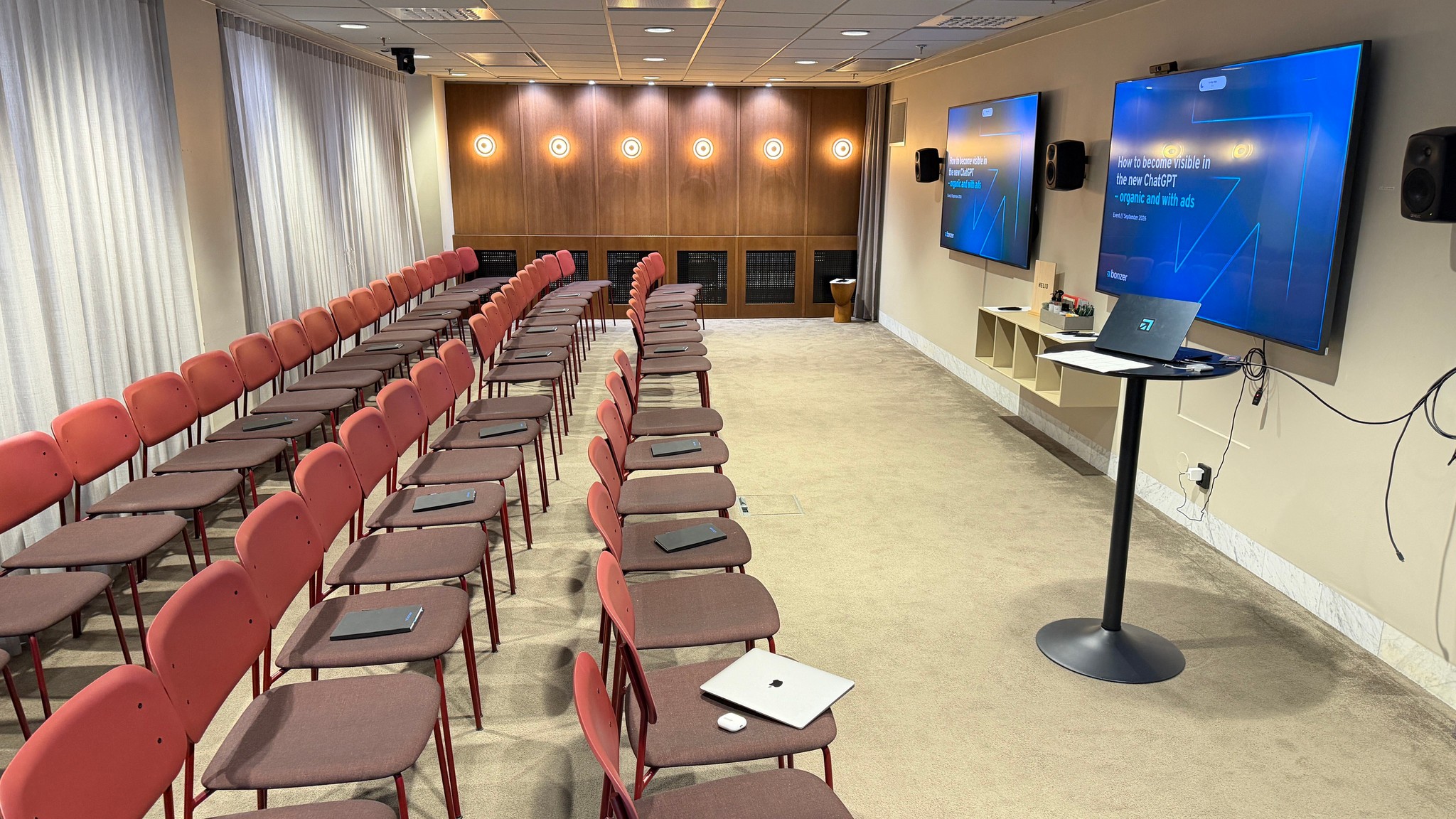 Konferencelokale klar til foredrag med skærme, der viser "How to become visible in the new ChatGPT"